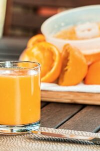 Glass of fresh orange juice with sliced oranges on wooden table, perfect for breakfast and healthy living.
