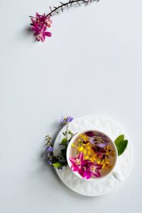 Aesthetic overhead view of floral tea with vibrant orchids in a white cup on a minimalist background.