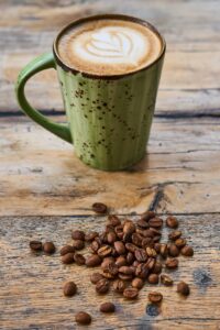 A green mug of cappuccino with coffee beans on a rustic wooden surface.