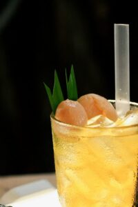 Chilled lychee cocktail in glass with ice, garnished with a straw and greenery.